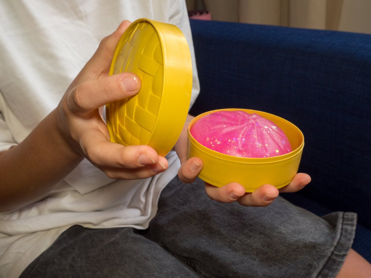 A child's hands unboxing a sparkly pink squishy dumpling from a little yellow steamer basket